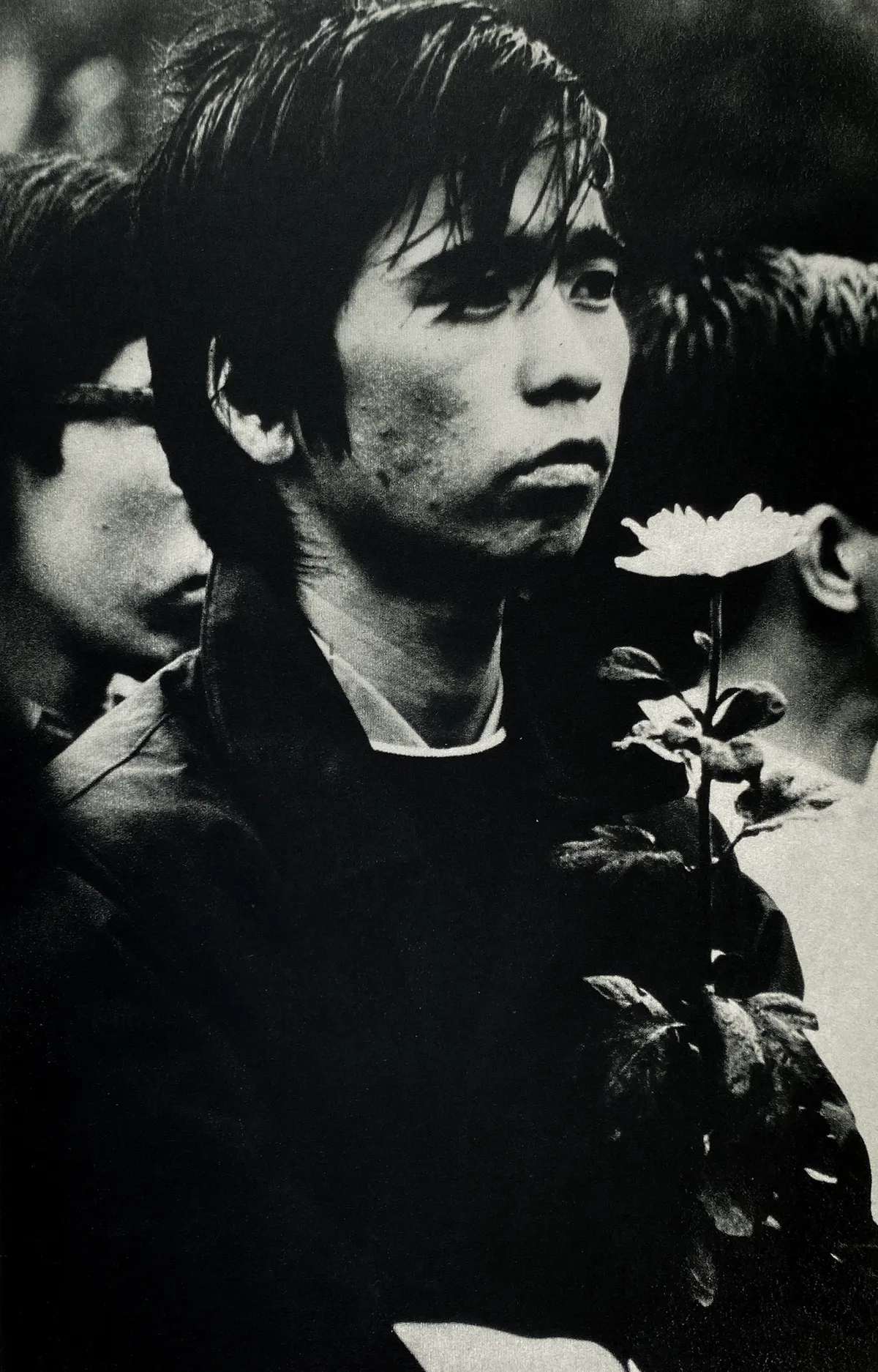 Fotografia en blanc i negre. Un jove amb posat trist porta una flor blanca a la mà.