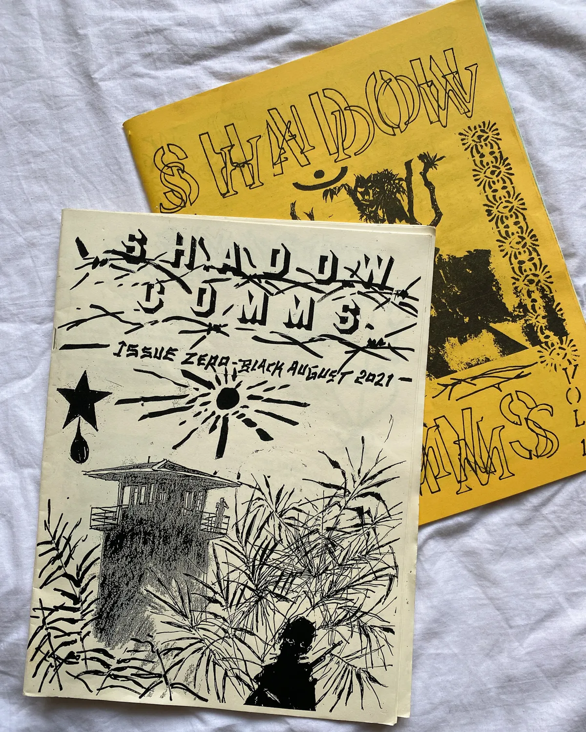 Fotografia de les dues primeres edicions de Shadow Comms, una sobre l'altra sobre un fons blanc